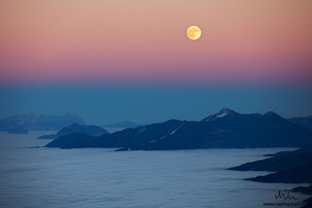 Vollmond über Bergen, die wirken wie Inseln in einem Meer aus Nebel